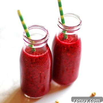 Two cherry pineapple smoothies in small bottles with green and yellow straws.