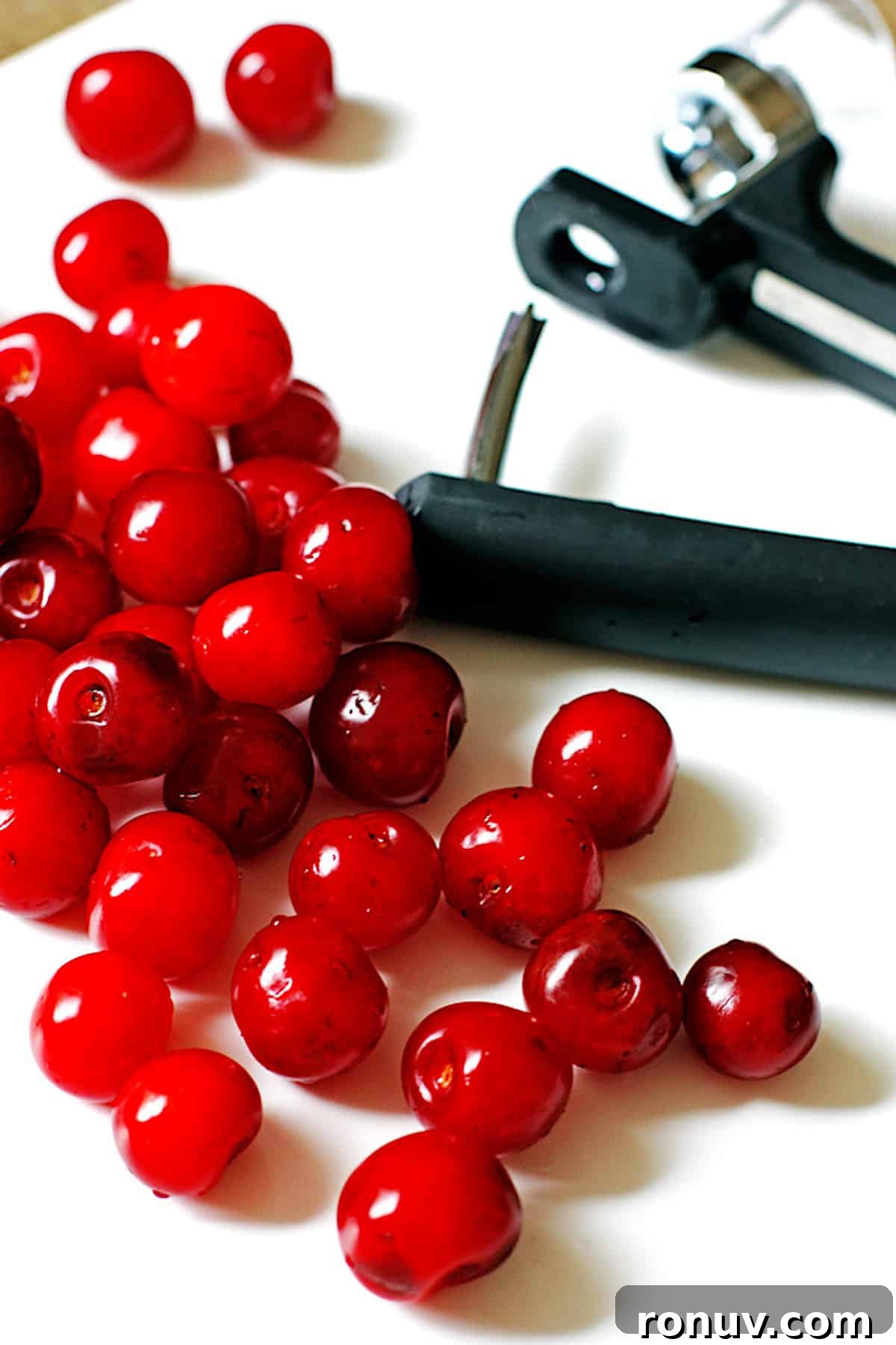 Tart cherries and a cherry pitter on a white counter.