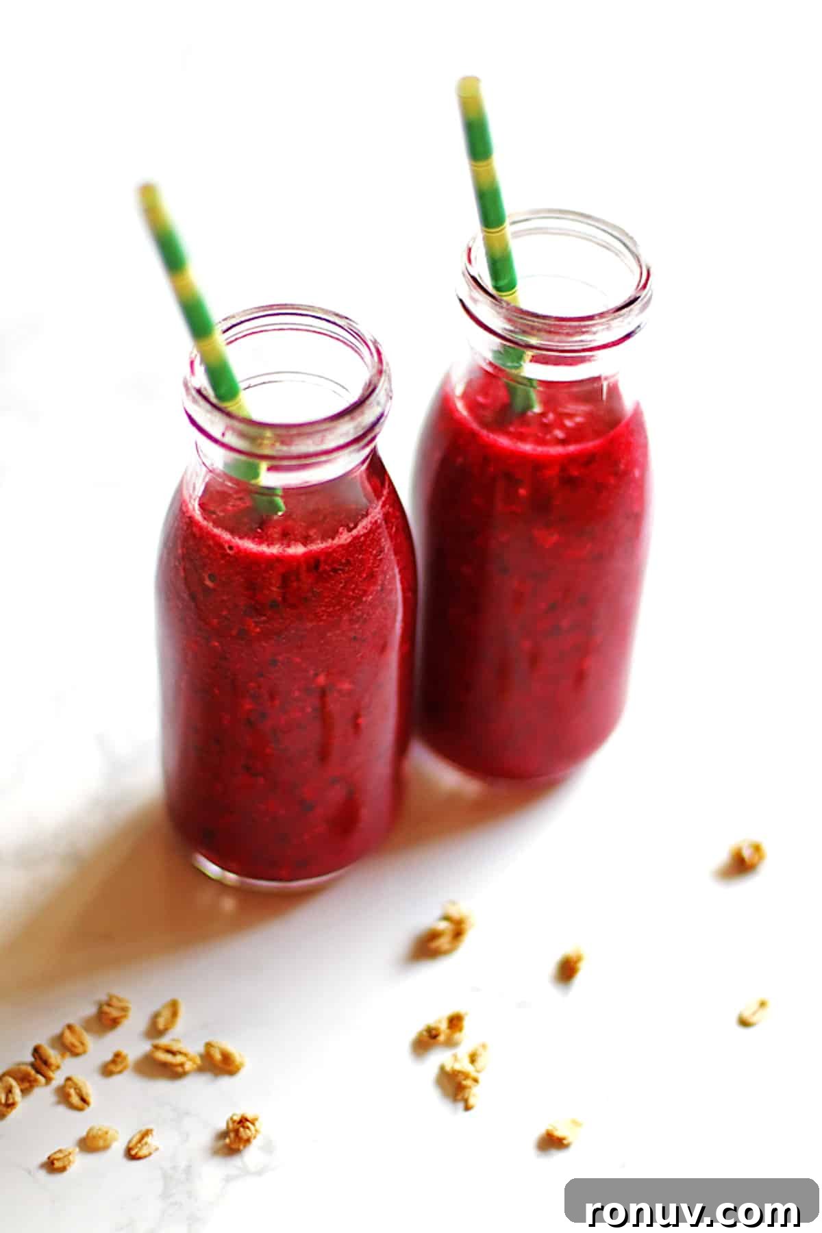 Two cherry pineapple smoothies in small bottles with green and yellow straws.