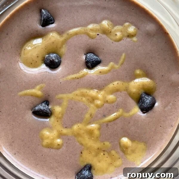 A chocolate peanut butter and banana smoothie with peanut butter drizzled over the top and chocolate chips sprinkled around.