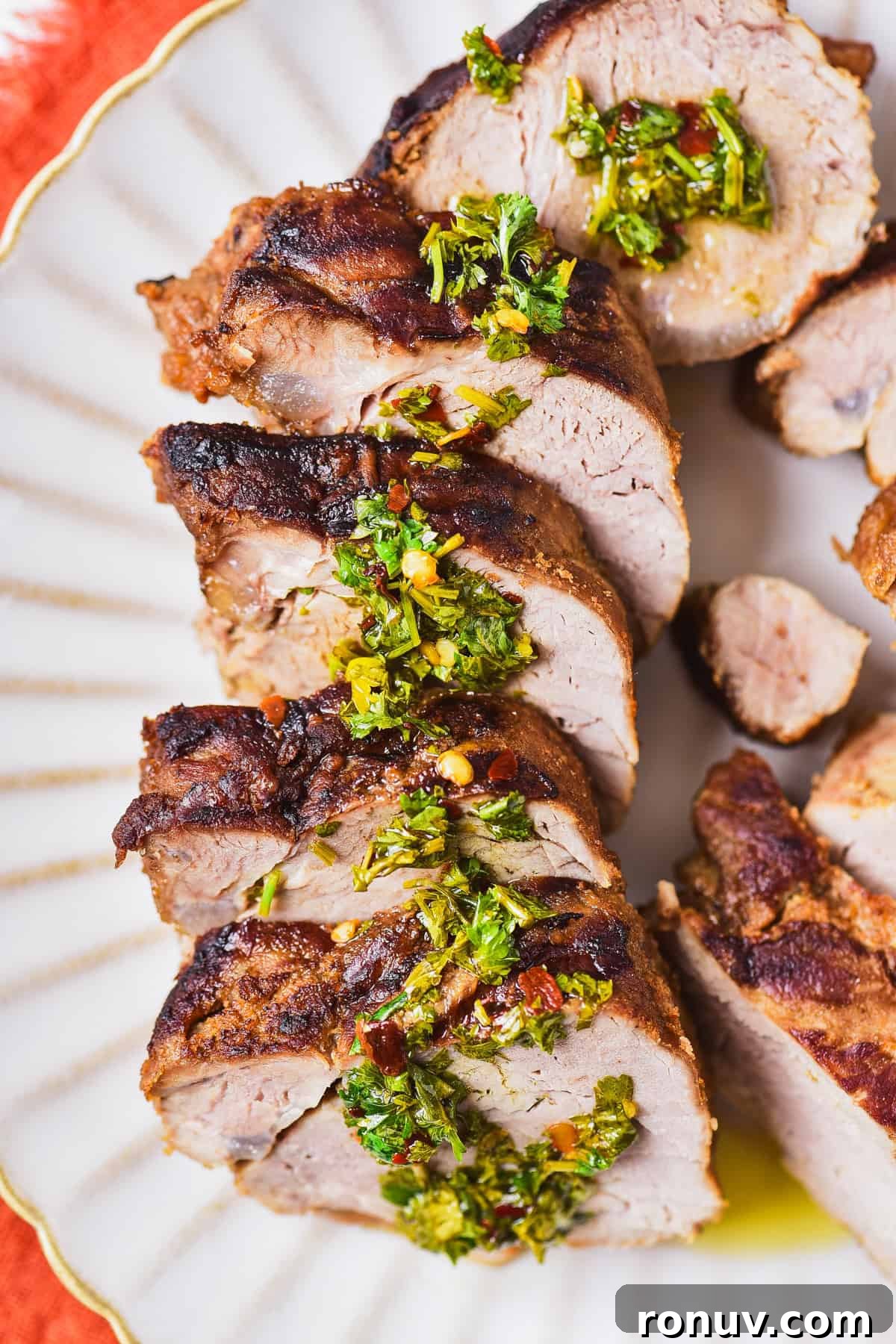 Juicy Marinated Grilled Pork Tenderloin Recipe 10 Sliced pork tenderloin on a plate with fresh herb sauce.