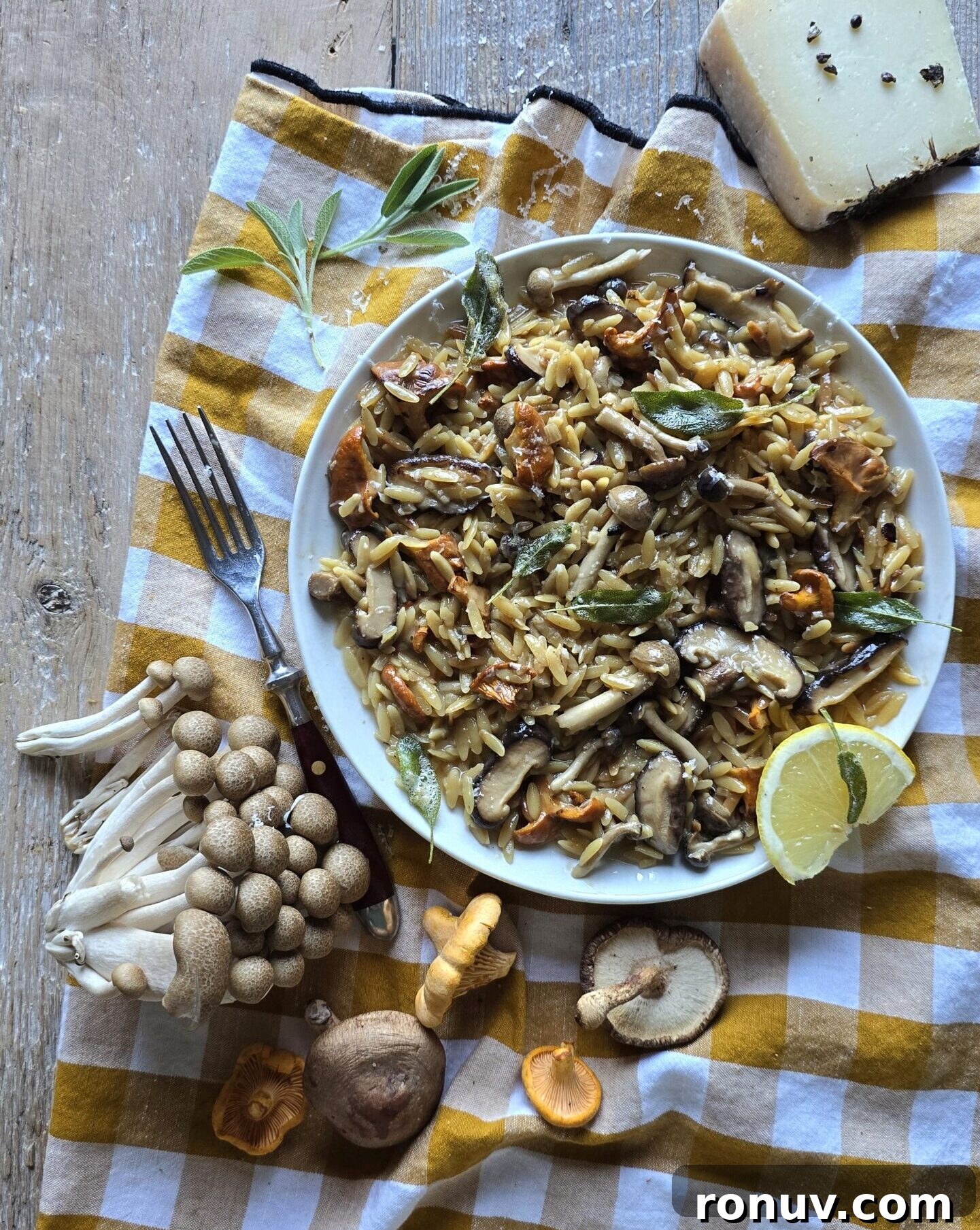 Brown Butter Mushroom Orzo with Crispy Sage 4 A plate of Mushroom Orzo with Brown Butter Crispy Sage sits on a tea towel, surrounded by fresh mushrooms and a block of cheese.