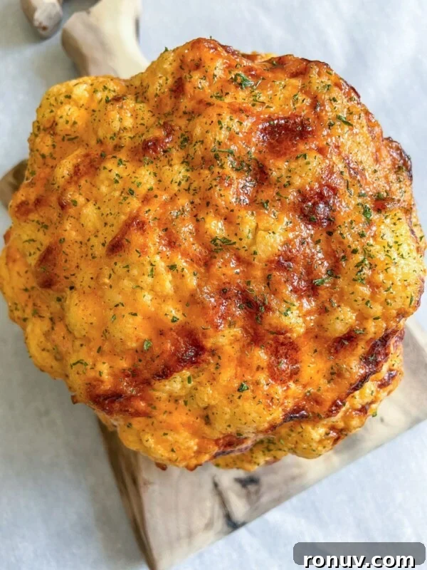 Whole roasted cauliflower head with golden-brown crust on a wooden board.
