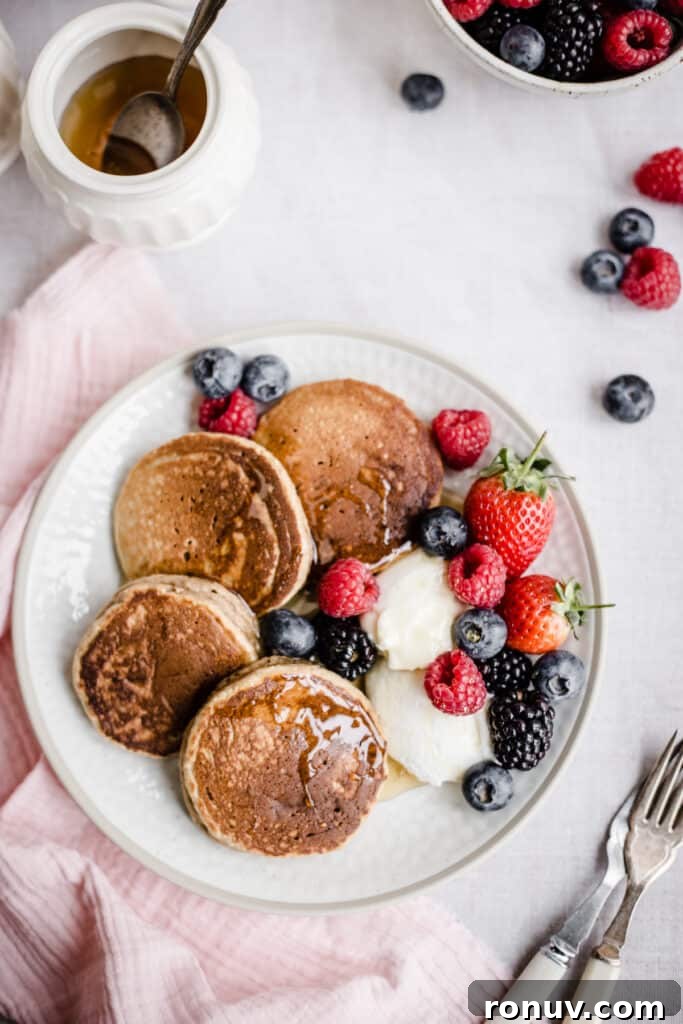Fluffy Gluten-Free American Pancake Recipe 3 Pancakes on a plate with berries next to bowl of fruit, forks and honey pot
