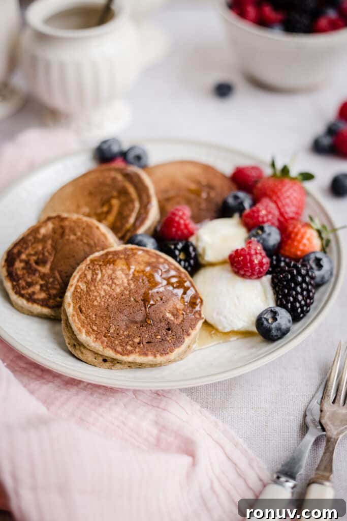 Fluffy Gluten-Free American Pancake Recipe 9 Pancakes on a plate with berries next to bowl of fruit, forks and honey pot