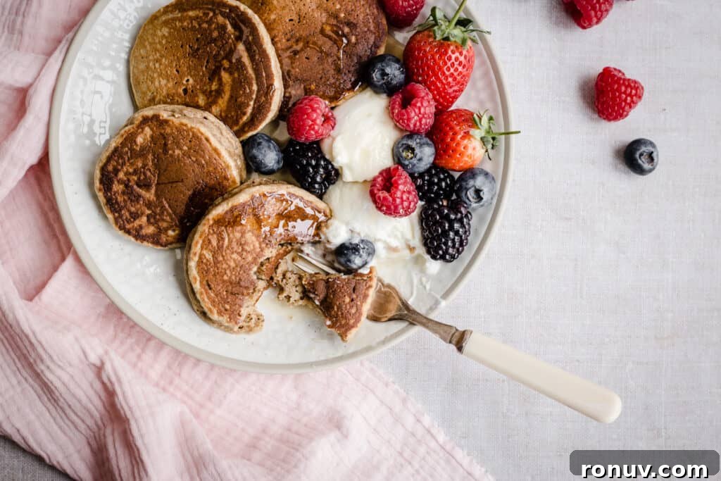 Fluffy Gluten-Free American Pancake Recipe 10 Pancakes on a plate with berries with a forkful taken out.