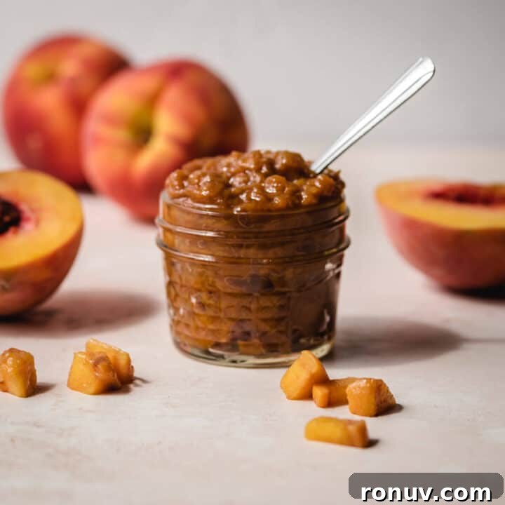 Small pieces of peach around a glass jar of peach jam.