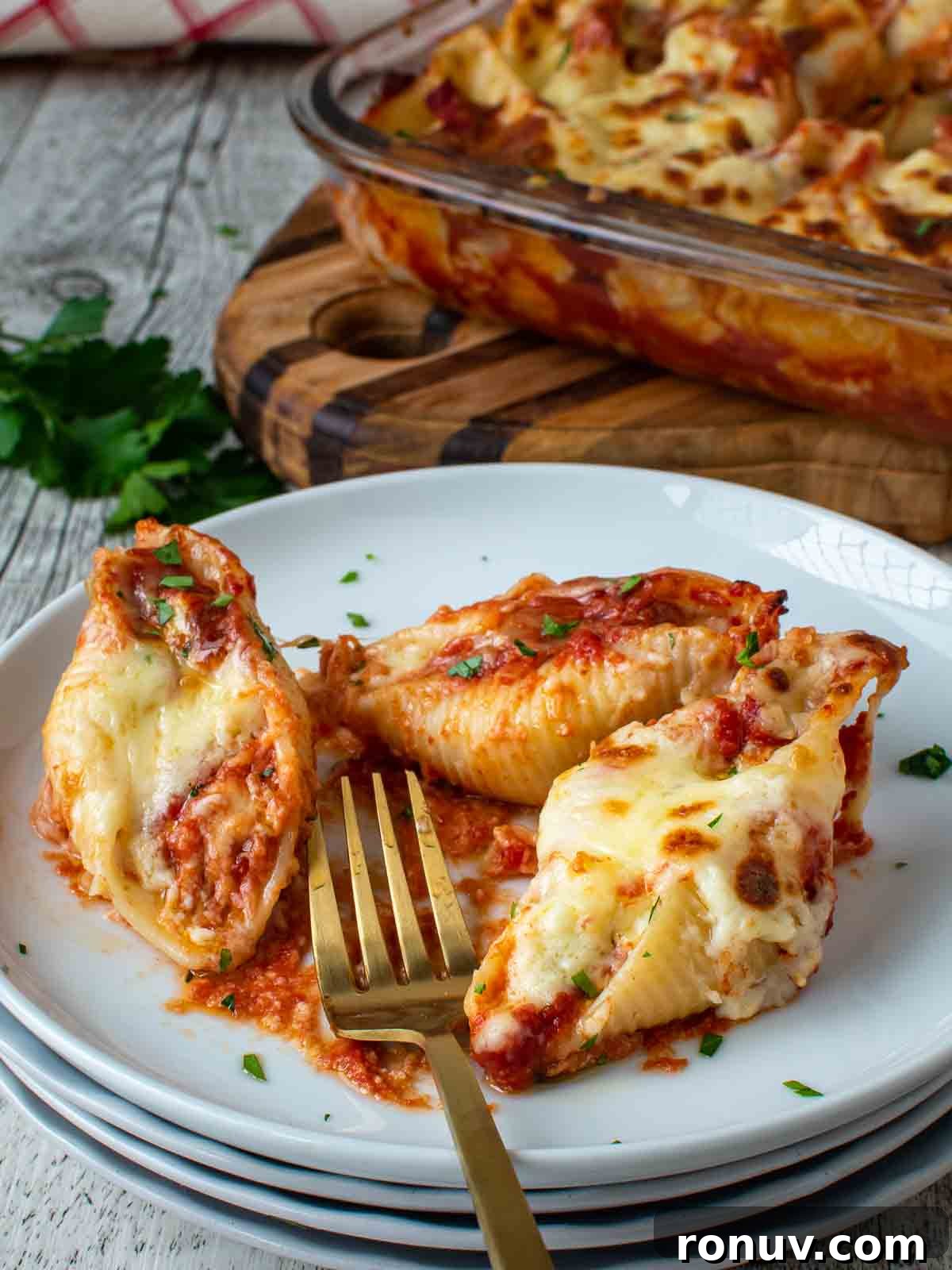 Ricotta-Stuffed Pasta Shells Recipe 2 Three pasta shells stuffed with ricotta on a stack of white plates with a gold fork.