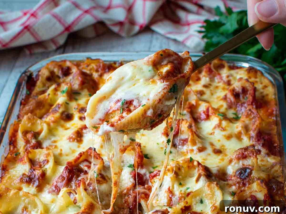 Ricotta-Stuffed Pasta Shells Recipe 14 A filled pasta shell being lifted from a pan full of pasta shells with cheesy string pulls.