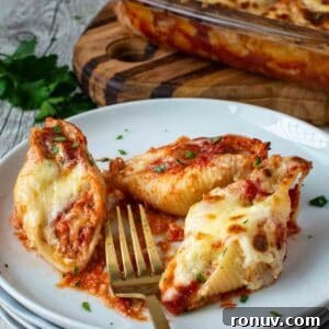 Ricotta-Stuffed Pasta Shells Recipe 15 Three giant cheese stuffed shells on a stack of white plates with a gold fork.