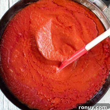 Ricotta-Stuffed Pasta Shells Recipe 9 Tomato pasta sauce in a black skillet being stirred with a red spatula.