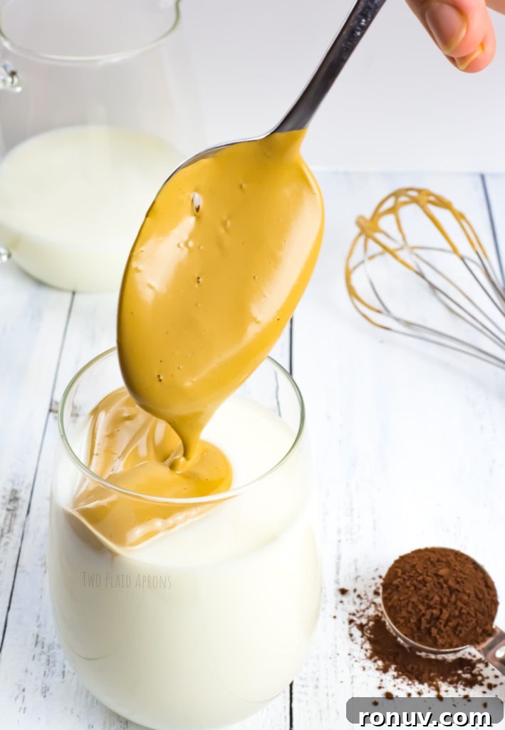 Dalgona Coffee Recipe: Whipped Coffee at Home 5 Spooning a scoop of whipped coffee mixture on top of milk.