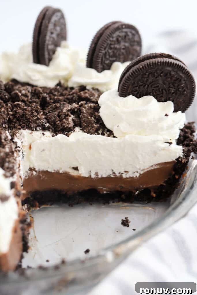 Classic Chocolate Cream Pie Recipe 2 Oreo pudding pie in a pie plate with a slice removed, topped with whipped cream and Oreo cookies.
