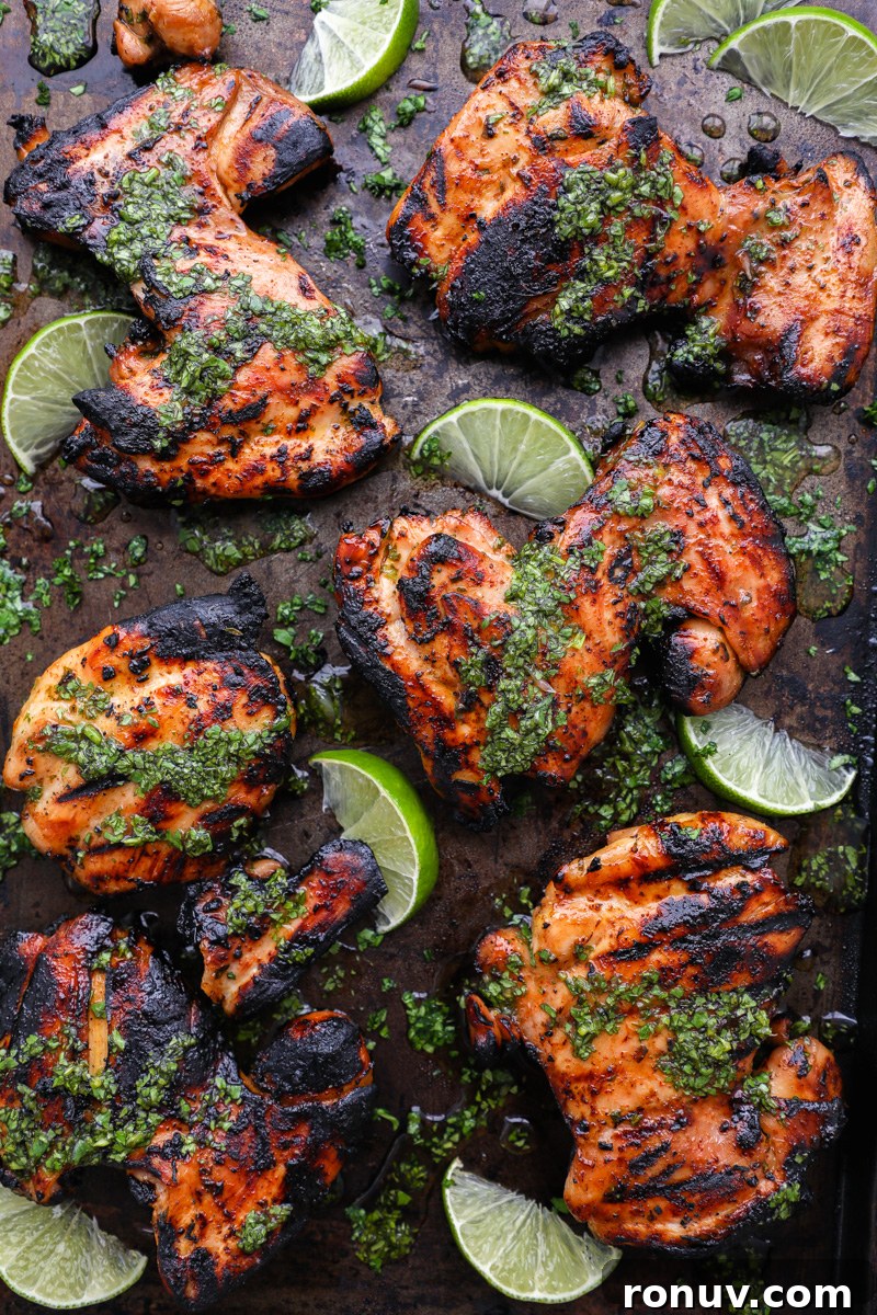 A large tray filled with honey lime grilled chicken thighs surrounded by fresh lime wedges