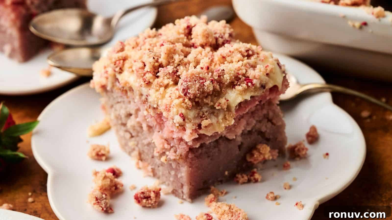 21 Strawberry Recipes to Savor Strawberry Season 13 A slice of crumb-topped strawberry coffee cake sits on a white plate with a spoon beside it; additional cake and plates are in the background.