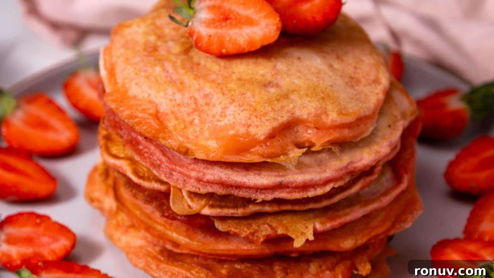 21 Strawberry Recipes to Savor Strawberry Season 17 A stack of pancakes topped with sliced strawberries, surrounded by more strawberries on a plate.