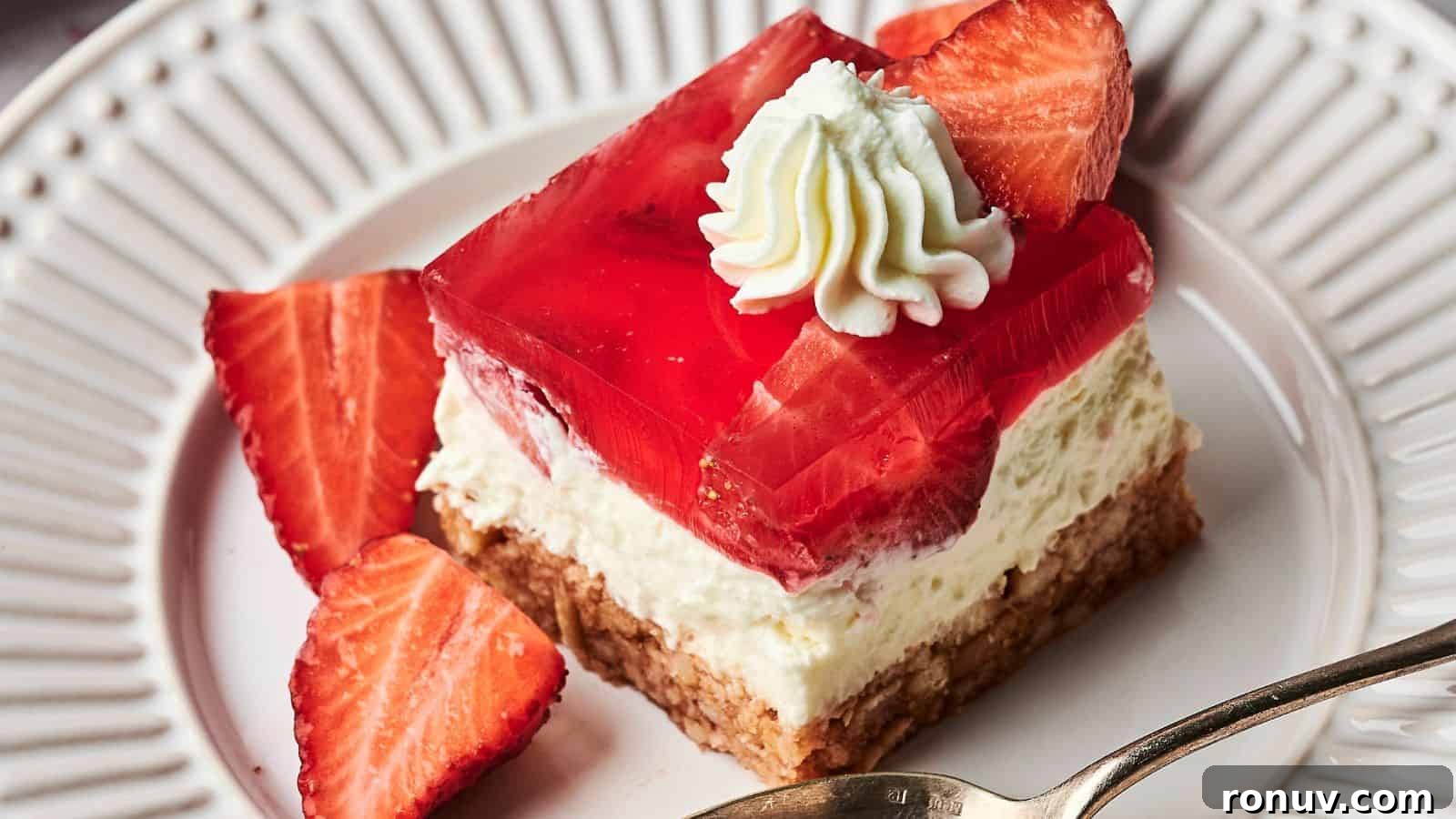 21 Strawberry Recipes to Savor Strawberry Season 18 A dessert with a crumbly crust, creamy filling, a layer of red gelatin, topped with a whipped cream dollop and a strawberry slice, on a white plate with a spoon.