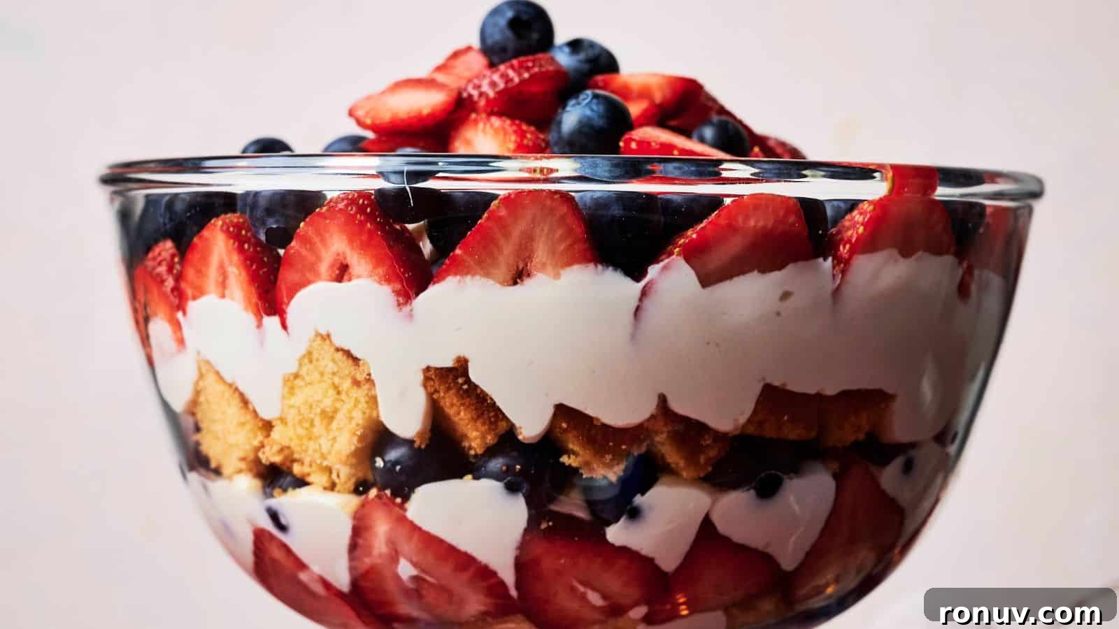 21 Strawberry Recipes to Savor Strawberry Season 6 A glass bowl filled with layered dessert, featuring sliced strawberries, blueberries, whipped cream, and cake pieces.