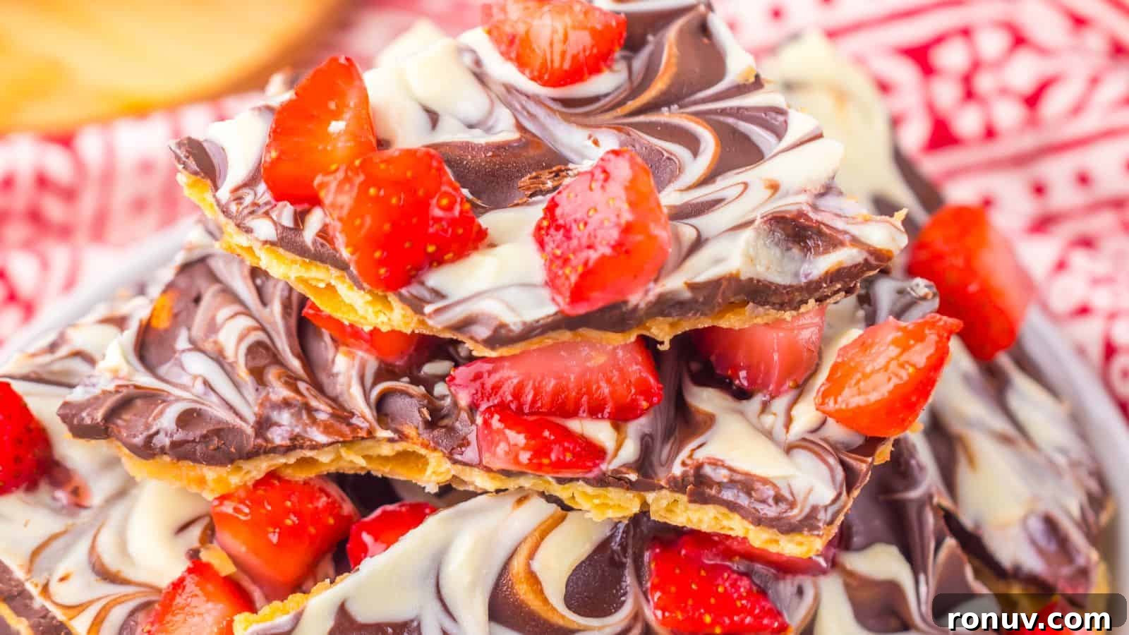 21 Strawberry Recipes to Savor Strawberry Season 7 Stack of chocolate bark with swirled dark and white chocolate, topped with fresh sliced strawberries, on a red patterned cloth background.