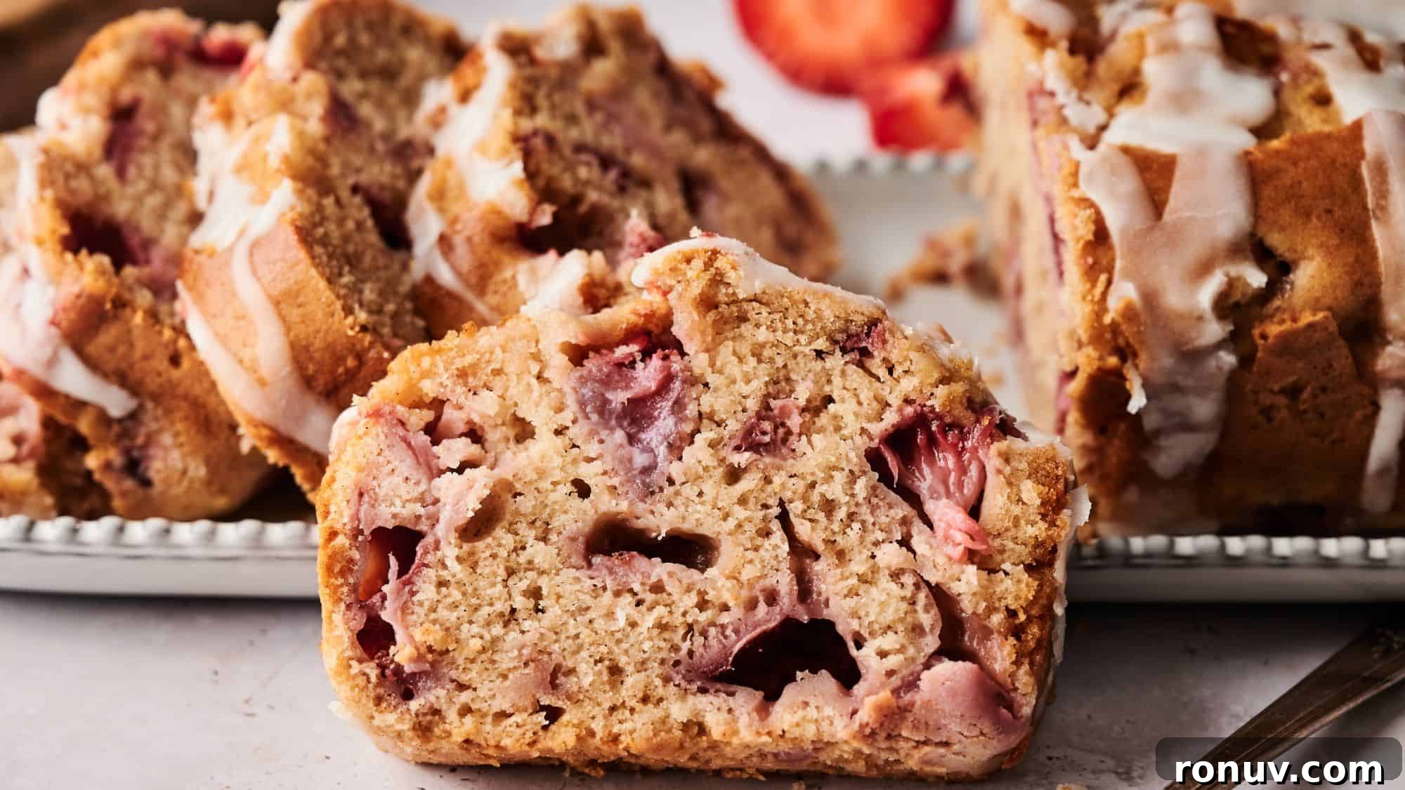 21 Strawberry Recipes to Savor Strawberry Season 10 A close-up of sliced strawberry bread with visible strawberry pieces and a drizzle of white icing on top, arranged on a plate.