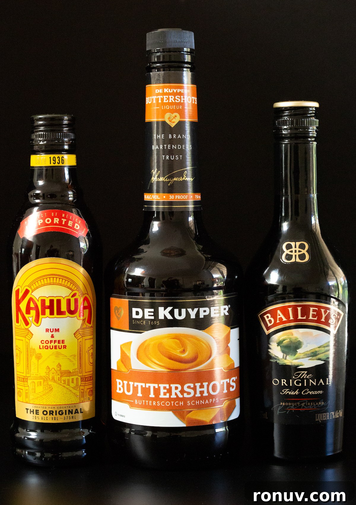Butterfinger Shot Recipe: Candy Bar Cocktail 3 A bottle of Kahlua, Buttershots, and Bailey's Irish Cream on a black background.