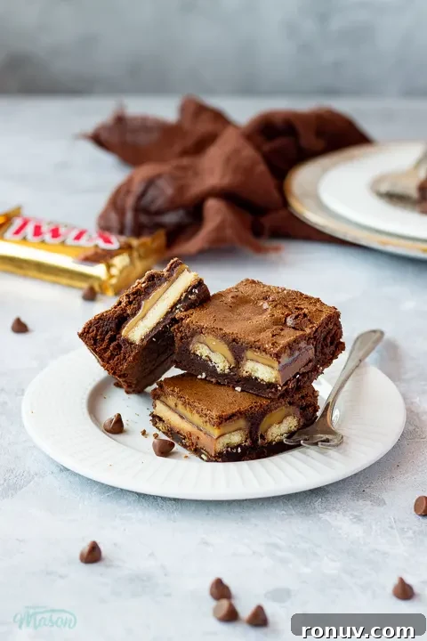 Homemade Fudgy Twix Brownies Recipe 7 3 Twix brownies and a fork stacked on a white ribbed plate over a mottled grey backdrop.