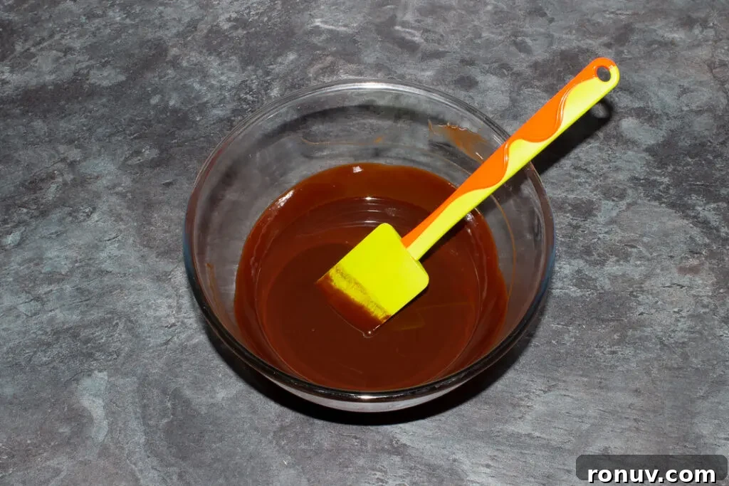 Homemade Fudgy Twix Brownies Recipe 10 Melted butter and dark chocolate in a glass mixing bowl with a green spatula.
