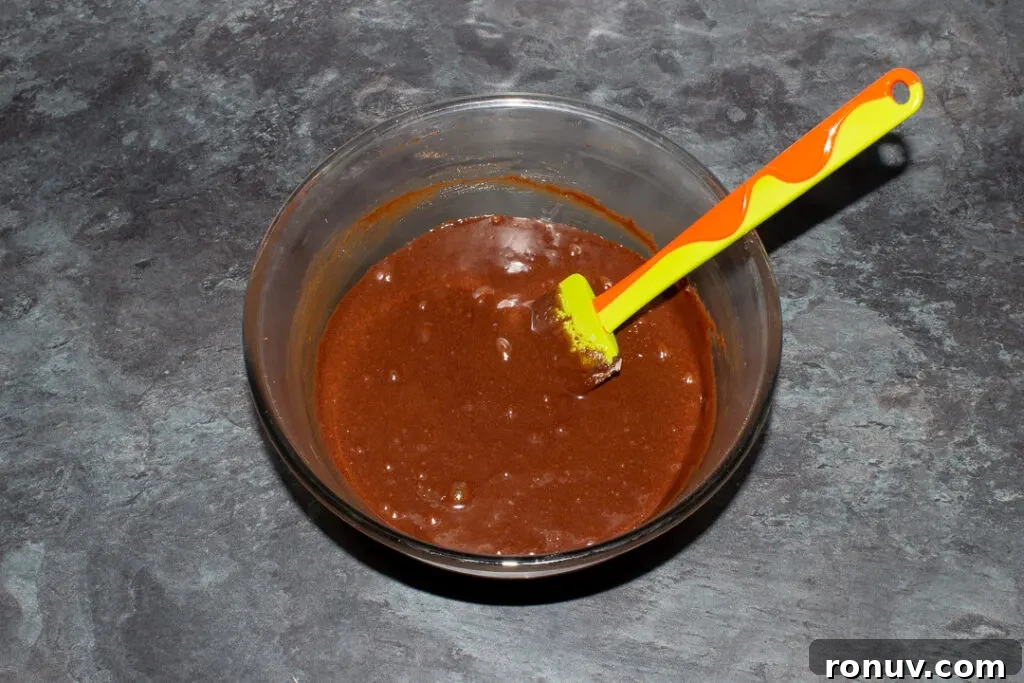 Homemade Fudgy Twix Brownies Recipe 12 Twix brownie batter in a glass mixing bowl with a green spatula.