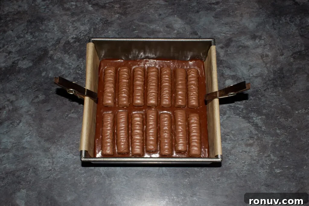 Homemade Fudgy Twix Brownies Recipe 13 Brownie batter topped with whole Twix bars in a lined square baking tin.