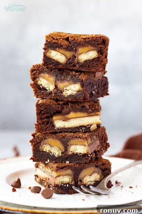 Homemade Fudgy Twix Brownies Recipe 16 A stack of 5 Twix brownies on a white ribbed plate with a fork set over a grey mottled backdrop.