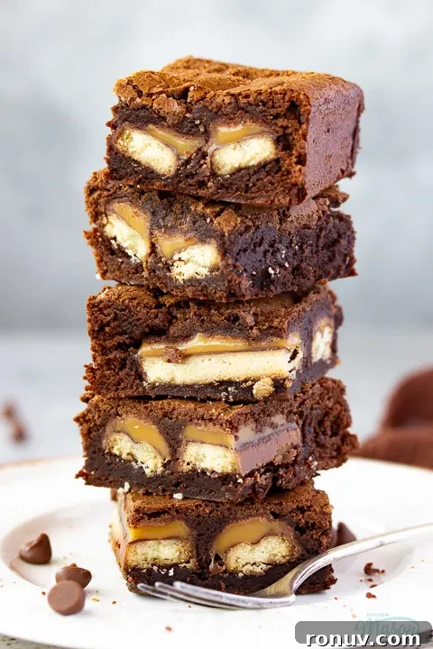 Homemade Fudgy Twix Brownies Recipe 3 Close up of a stack of 5 Twix brownies on a white ribbed plate with a fork set over a grey mottled backdrop.
