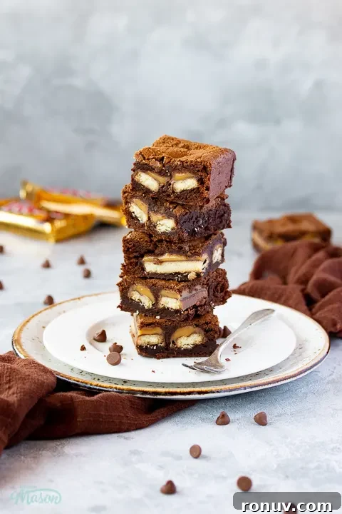 Homemade Fudgy Twix Brownies Recipe 4 A stack of 5 Twix brownies on a white ribbed plate with a fork set over a grey mottled backdrop.