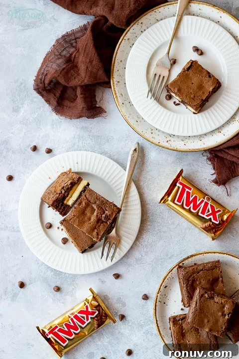 Homemade Fudgy Twix Brownies Recipe 5 Flat lay view of 3 Twix brownies and a fork stacked on a white ribbed plate over a mottled grey backdrop.
