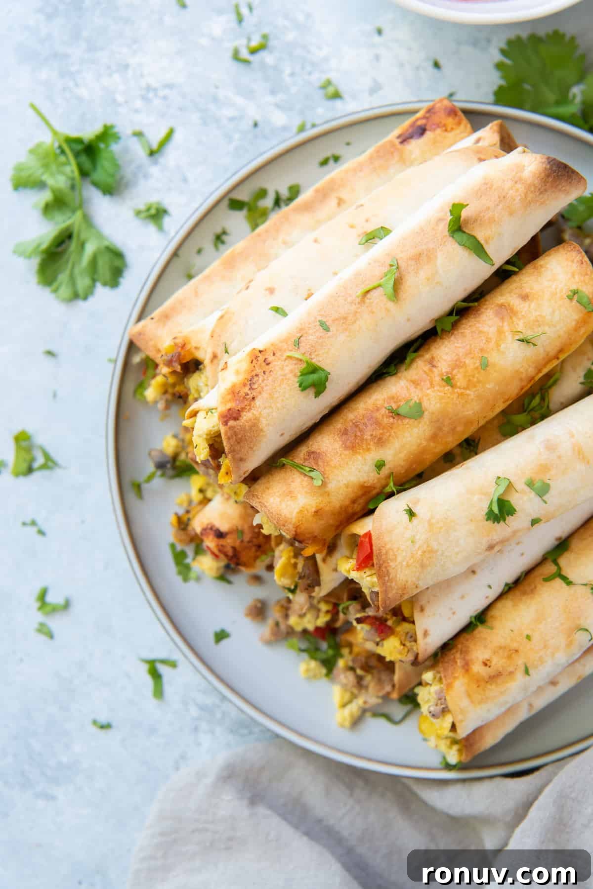 Crispy Oven-Baked Breakfast Taquitos Recipe 3 A top down shot of breakfast taquitos stacked on a white plate.