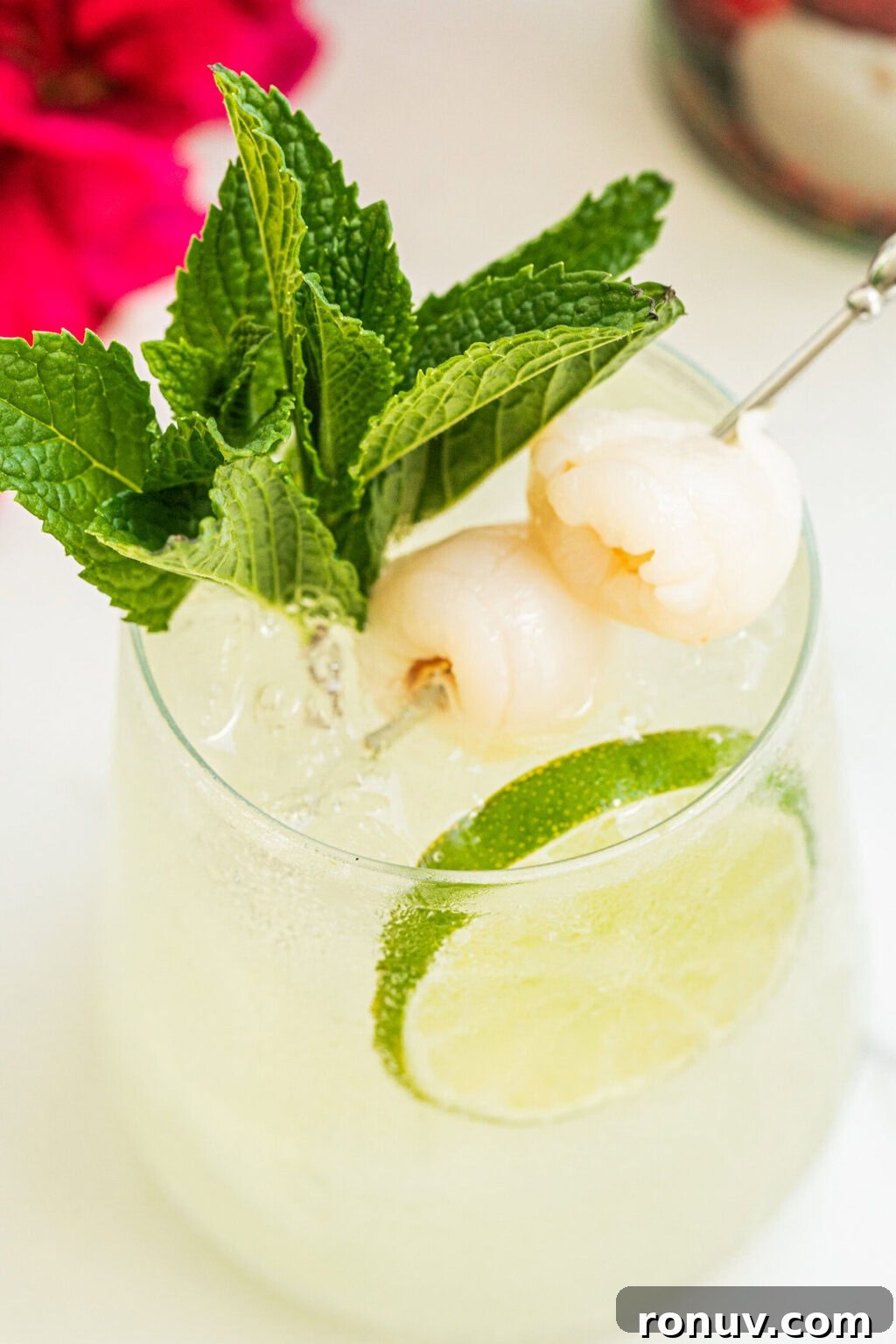 a stemless wine glass with lychee cocktail spritz, two lychee fruits, a sprig of fresh mint and a lime wheel
