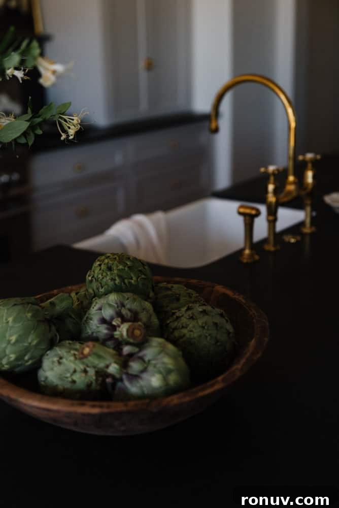 Granite Countertops: Pros, Cons, and Cost Guide 2 artichokes in wooden bowl on black granite countertop with brass faucet and white sink in background
