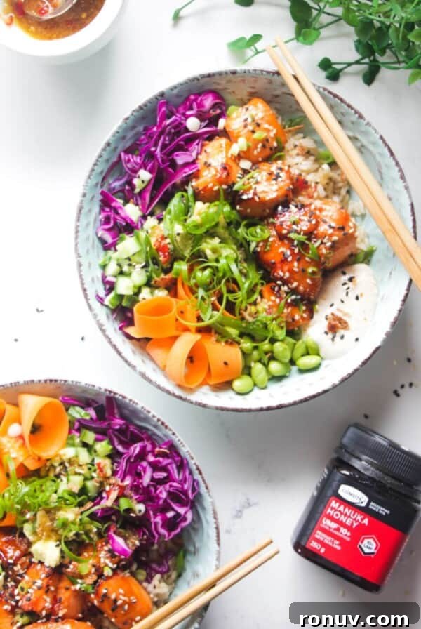 Two baked salmon poke bowls on a marble background with honey on the side.