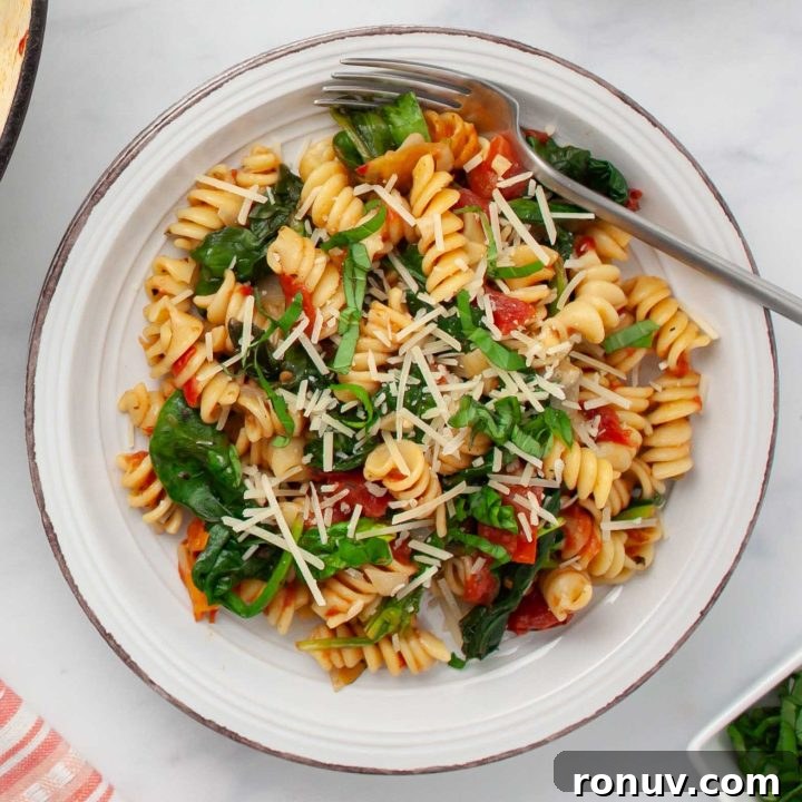 Plate of tomato Spinach Pasta garnished with Parmesan cheese and fresh basil strips.