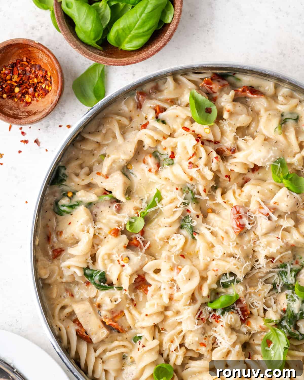 30-Minute Creamy Marry Me Chicken Pasta Recipe 14 A pan filled with marry me chicken pasta that has been garnished with basil leaves, red pepper flakes and freshly grated cheese.