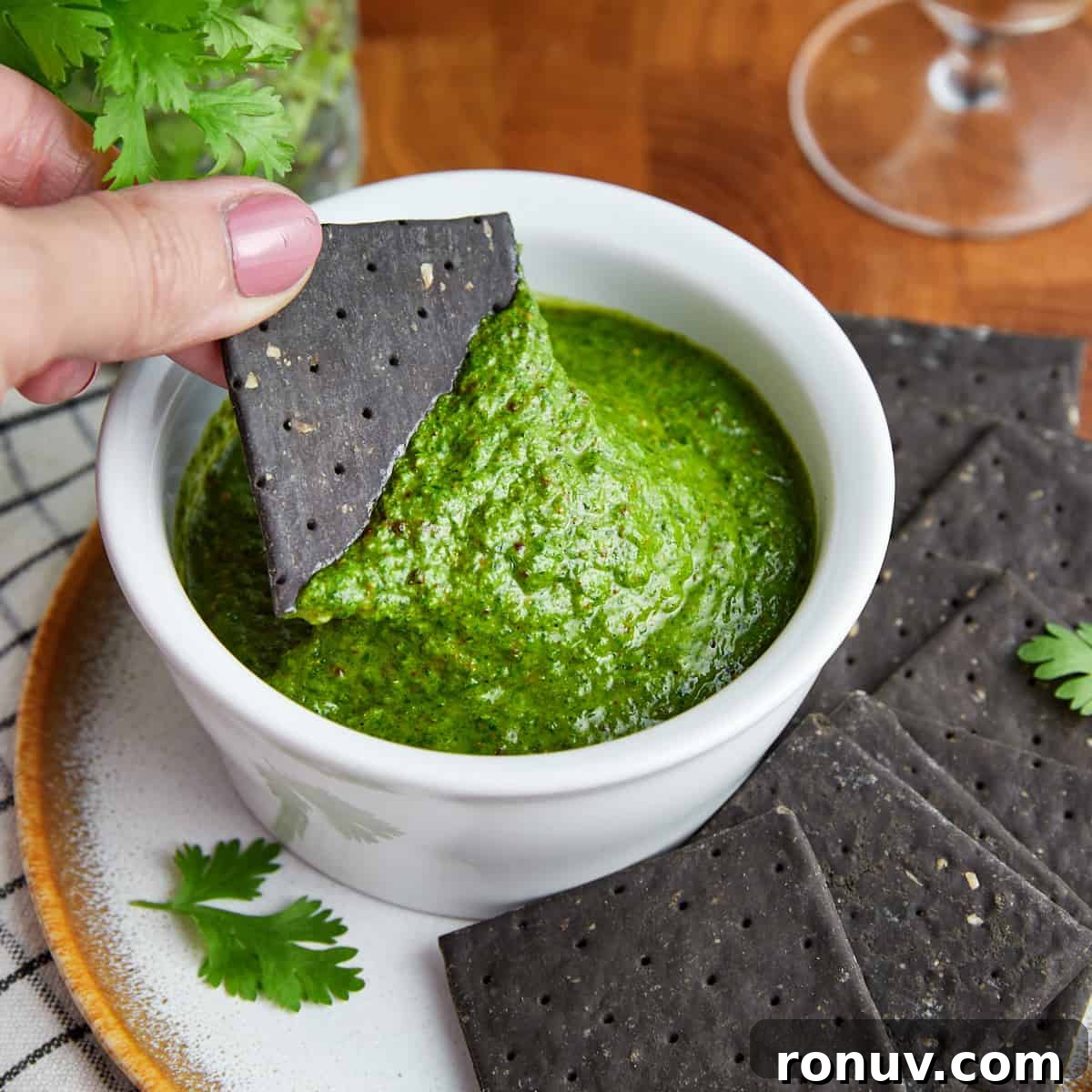 Photo of a bowl of zhoug on a plate with black crackers.