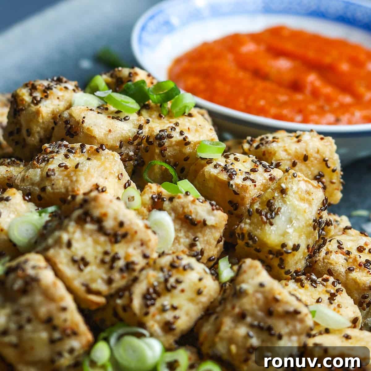 Crispy Air Fryer Tofu Recipe with Chia Seeds 4 Close-up image showing crispy air fried tofu with sliced spring onions sprinkled on top and a bowl of kimchi sauce in the background.