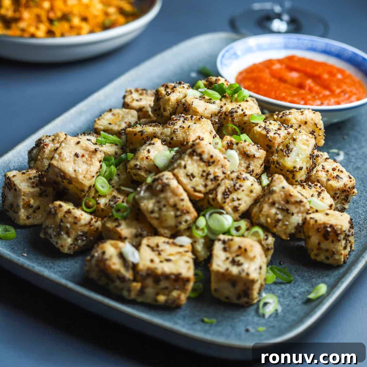 Crispy Air Fryer Tofu Recipe with Chia Seeds 8 Blue grey plate filled with crispy chia tofu cubes sprinkled with sliced spring onions and served with a little bowl of kimchi sauce.