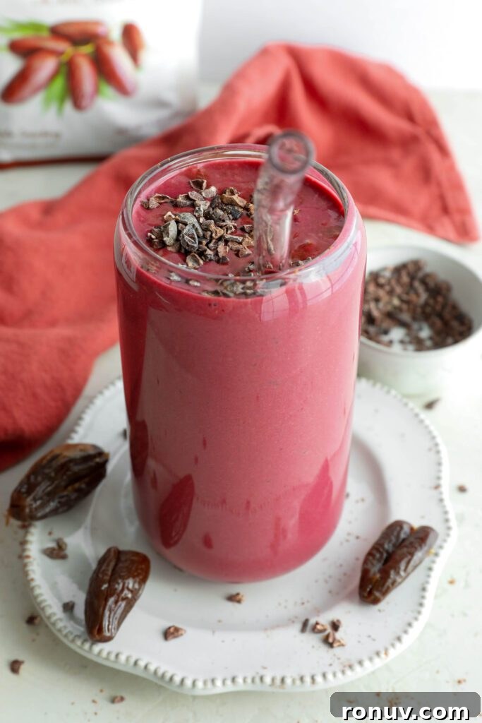 Creamy Red Velvet Protein Shake Recipe 10 Red Velvet Protein Shake served on a plate with a straw and Medjool dates and cacao nibs on plate by Flora & Vino