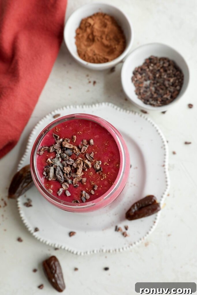 Creamy Red Velvet Protein Shake Recipe 9 Red Velvet Protein Shake served on a plate with a straw and Medjool dates and cacao nibs on plate by Flora & Vino