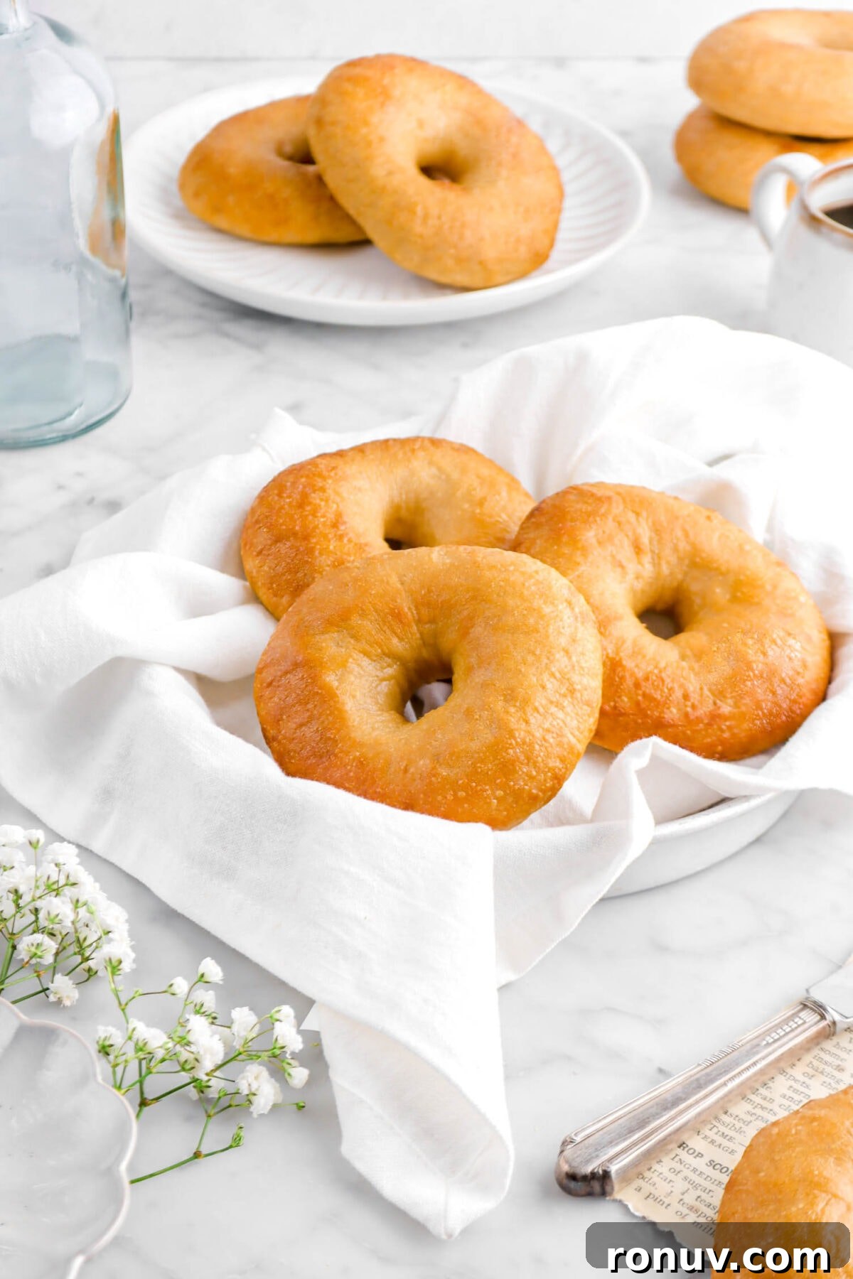 How to Make Sourdough Bagels at Home 9 close up o three bagels on white napkin with two bagels on white plate and two more stacked bagels behind