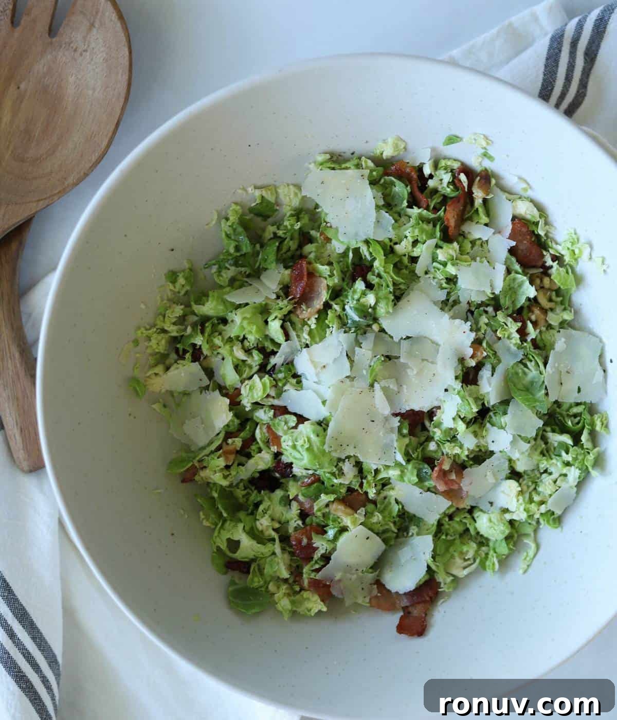 Shaved Brussels Sprouts Salad with Crispy Bacon 2 Shaved brussel sprout salad in salad bowl topped with parmesan cheese.