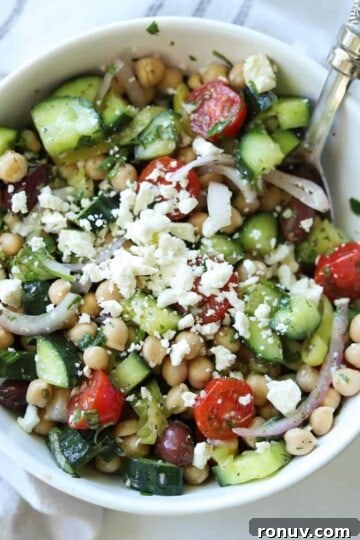 mediterranean cucumber tomato salad in a white bowl with large spoon.