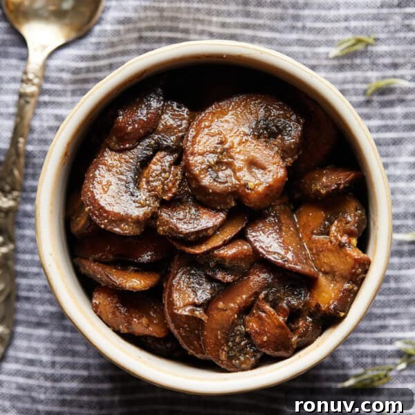 Overhead photo of browned sliced mushrooms in a small bowl on a striped cloth.