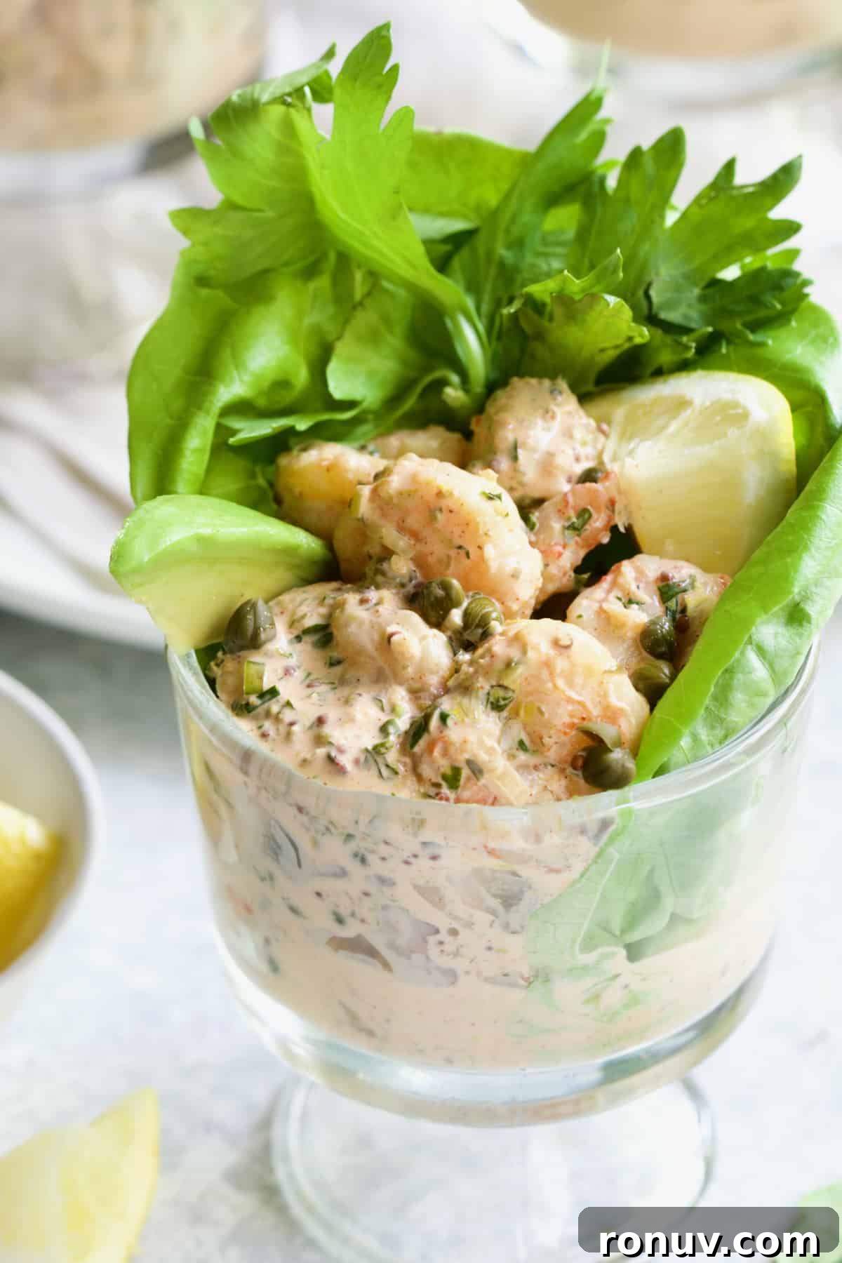 Spicy Shrimp Cocktail with Sriracha Remoulade 7 Sriracha Shrimp Remoulade Cocktail in footed glass with avocado, lemon, lettuce and celery sprigs.