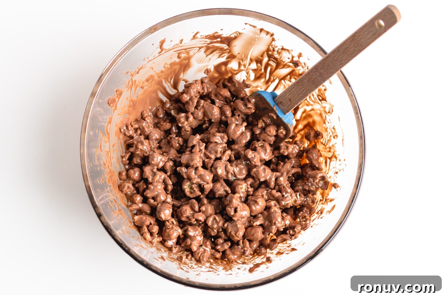 How to Make Chocolate Halloween Popcorn Balls 7 Popcorn and melted chocolate being mixed together in a glass bowl.